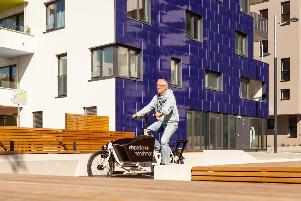 Ein Mann fährt auf dem Lastenrad durch das sonnige und verkehrsberuhigte Wohnquartier.