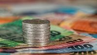 Man sieht eine Reihe Geldscheine, auf der ein Stapel Münzen steht