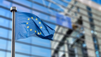 Das Bild zeigt eine wehende Europaflagge vor der Glasfassade des Europäischen Parlaments.