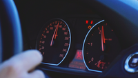 Das Bild zeigt eine Hand am Lenkrad sowie den dahinterliegenden Autotacho, der eine Geschwindigkeit von 130 km/h anzeigt. 