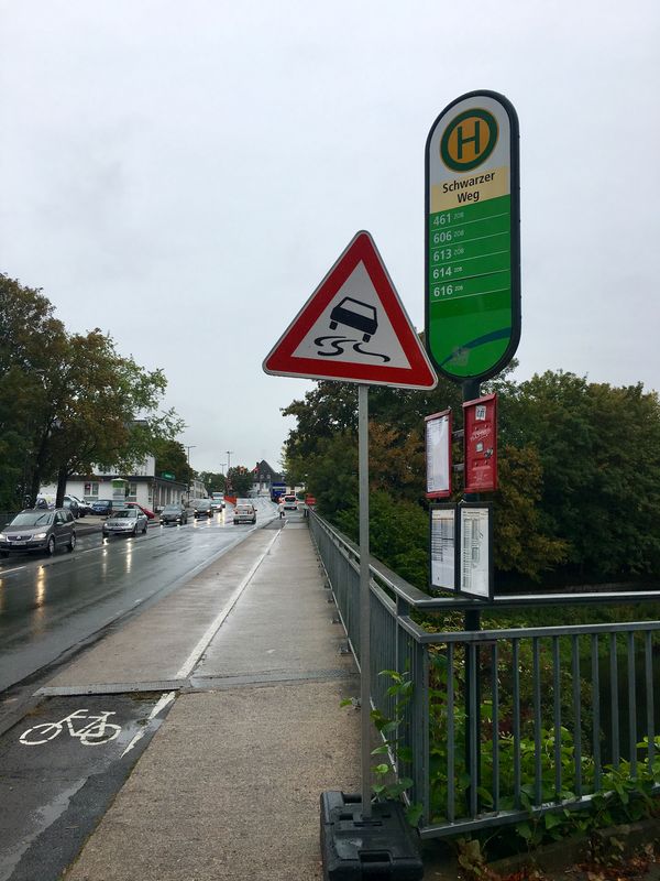 Auf dem Bild ist Straße auf einer Brücke zu sehen. Neben der Straße befindet sich ein Gehweg mit einem Haltestellenschild. Das Schild wird teilweise durch ein Verkehrszeichen verdeckt.