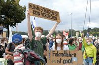 Ein junger Demonstrant hält ein Pappschild hoch auf dem steht "Klimaschutz ist kein Verbrechen". Neben ihn steht eine junge Demonstrantin mit einem Pappschild in der Hand, auf dem steht "Fahrradfahren ist cool".
