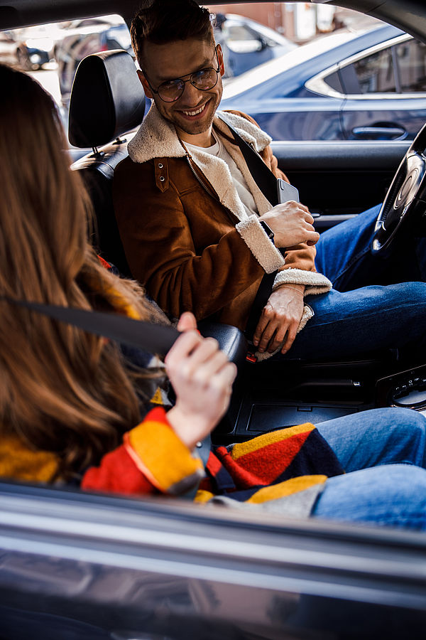 Foto: Fahrgäste sitzen im Auto, eine Person nutzt während der Fahrt ein Smartphone.