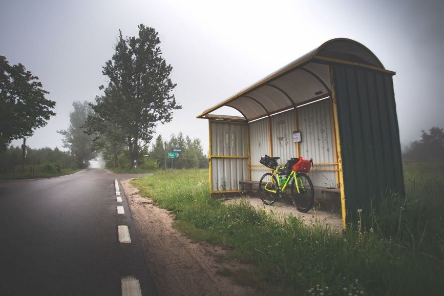 Symbolbild ÖPNV im ländlichen Raum: Foto einer Landstraße mit Bushaltestelle, unter der ein voll gepacktes Fahrrad steht