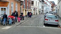 Am Rande einer gepflasterten Straße in Bremen laufen links Kinder über den Bürgersteig. Rechts parken Autos auf Parkplätzen. Die Gehwege bleiben frei.