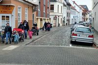 Am Rande einer gepflasterten Straße in Bremen laufen links Kinder über den Bürgersteig. Rechts parken Autos auf Parkplätzen. Die Gehwege bleiben frei.