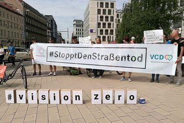 Menschen halten ein Banner hoch, auf dem #StopptDenStraßentod steht, davor ist auf Kartons auf dem Boden "Vision Zero" geschrieben.