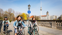 Das Bild zeigt fünf Jugendliche auf Fahrrädern, wie sie über eine Brücke fahren.