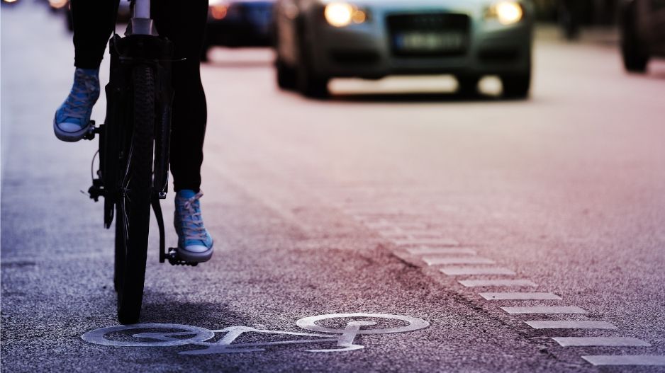 Eine Person auf dem Fahrrad, dahinter Autos.