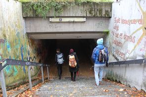 Drei Leute gehen eine Treppe, die zu einem Tunnel (Unterführung) führt, hinunter.