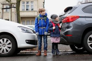 Zwei Schulkinder stehen zwischen Autos an der Fahrbahn