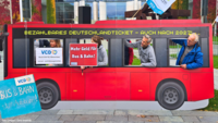 Bild zeigt Aktive und Mitarbeitende des VCD und Campacts vor dem Bundesverkehrsministerium in Berlin. Sie streiken für Preisstabilität und Sicherung des Deutschlandtickets auch über 2027 hinaus. Sie halten Schilder aus einem Bus, auf denen steht "Bus und Bahn statt Autobahn!", "Mehr Geld für den ÖPNV!" und "VCD - Mobilität für Menschen!". Auf dem Bus ist eine Anzeige mit dem Inhalt: Bezahlbares Deutschlandticket - Auch nach 2027!"