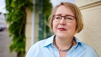 Das Bild zeigt Kerstin Haarmann, die auf einem Gehweg steht und an einer Hauswand lehnt.