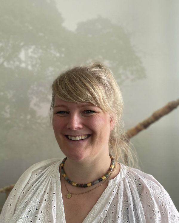 Foto: Frau mit blondem Haar und heller Bluse lächelt in die Kamera.