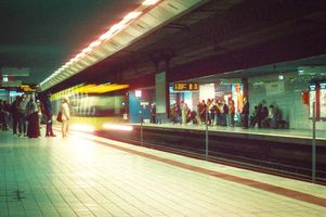 Durch lange Belichtung leicht unscharfes Foto einer U-Bahn die gerade in einen Bahnhof einfährt, Menschen warten am Bahnsteig