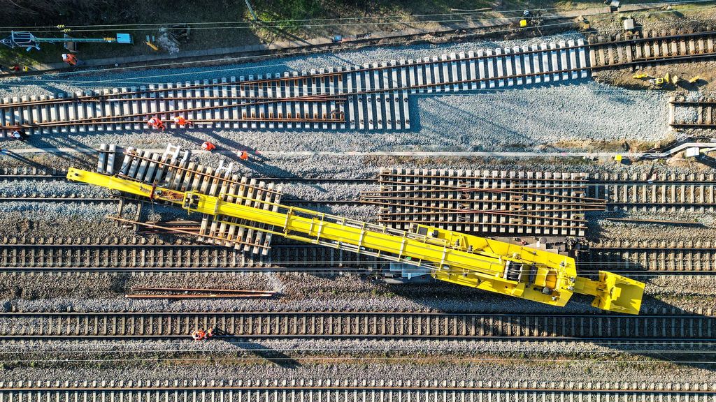Blick von oben auf viele nebeneinanderliegende Gleise. Darauf steht schräg ein gelbes Baustellenfahrzeug.