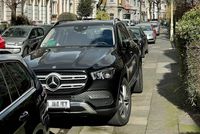Ein sehr großes Auto parkt halb auf dem Gehweg.