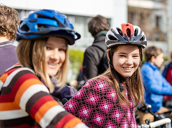 Foto: Zwei junge Radfahrerinnen mit Fahrradhelmen bei einer Veranstaltung im öffentlichen Raum.