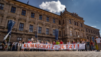Vor einem Gebäude aus dem 19. Jahrhundert demonstrieren Menschen mit dem Banner "Klimaschutz jetzt!"