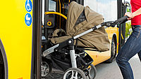 Das Bild zeigt eine Frau von der Seite, die einen Kinderwagen über eine Rampe in einen Bus schiebt.