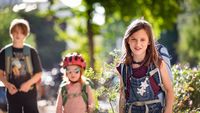 Drei Kinder und Jugednliche mit Schulranzen blicken lächelnd in die Kamera.