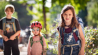 Drei Kinder und Jugednliche mit Schulranzen blicken lächelnd in die Kamera.
