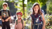 Drei Kinder und Jugednliche mit Schulranzen blicken lächelnd in die Kamera.