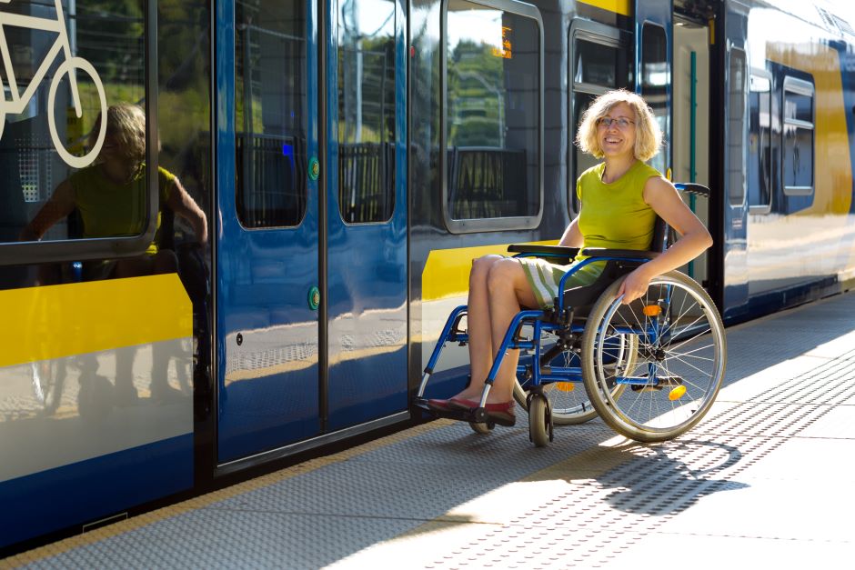 Fröhliche Frau im Rollstuhl vor einer Straßenbahn